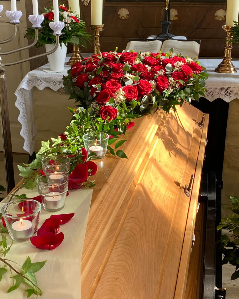 Sargschmuck aus roten Rosen auf hellem Sarg in der Kirche